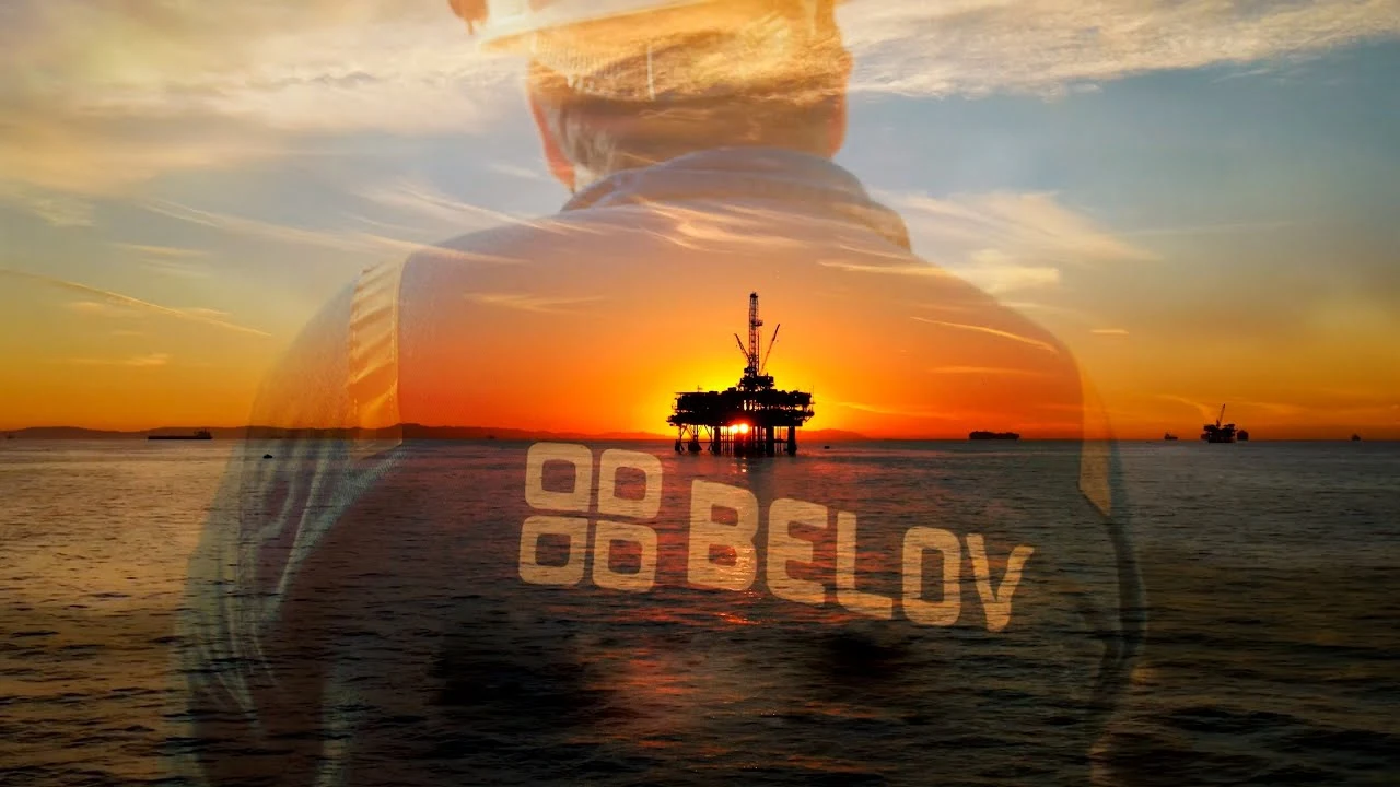 um homem parado na frente de uma grande plataforma de petróleo ao pôr do sol